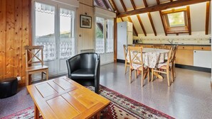 Une pièce chaleureuse avec un plafond en bois, une table à manger avec des chaises, un fauteuil en cuir noir et un coin cuisine équipé d’un réfrigérateur et d’un évier.