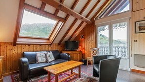 Une pièce chaleureuse avec un plafond en bois, un canapé en cuir noir, une table basse en bois et un téléviseur posé sur un meuble en bois.