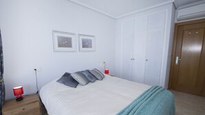 Ein Schlafzimmer mit einem Bett, einem Nachttisch, einer roten Lampe, einer türkisblauen Tagesdecke und einer Holztür.