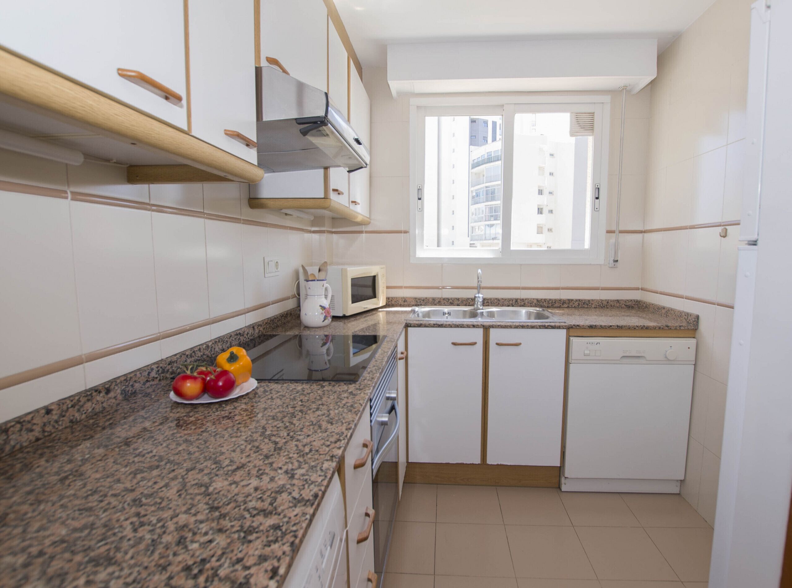 A compact kitchen with white cabinets, a granite countertop, a microwave, a sink, and a window with a view of buildings.