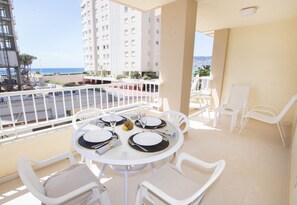 A balcony with a round table set for four, white chairs, and a view of the sea and buildings. - A57 EDIFICIO LA REINA 2º 12 (Calpe)