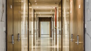 Un pasillo moderno y bien iluminado con paredes y puertas espejadas, que conduce a una habitación con un ventanal grande.