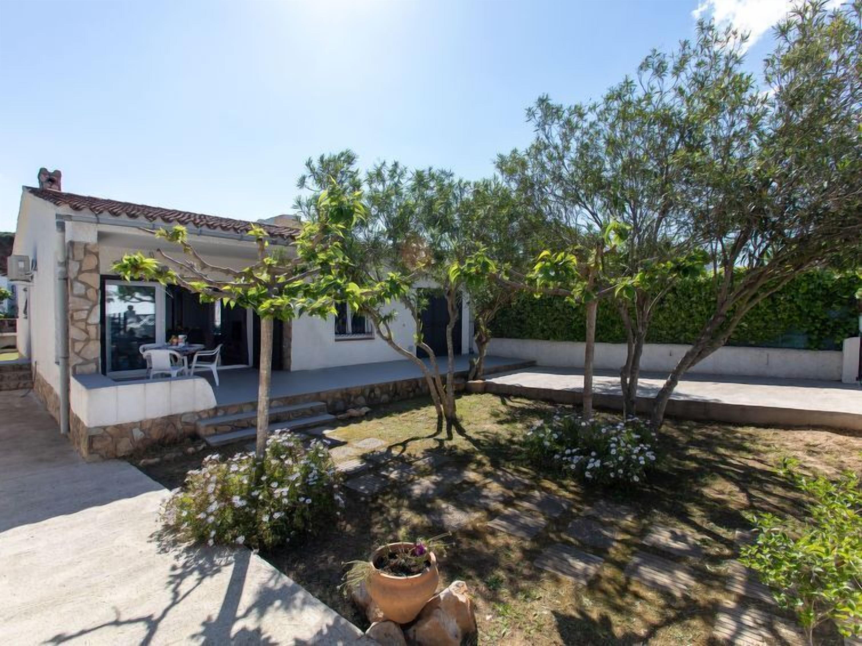 A modern house with a patio area, outdoor seating, and a garden with trees and plants.