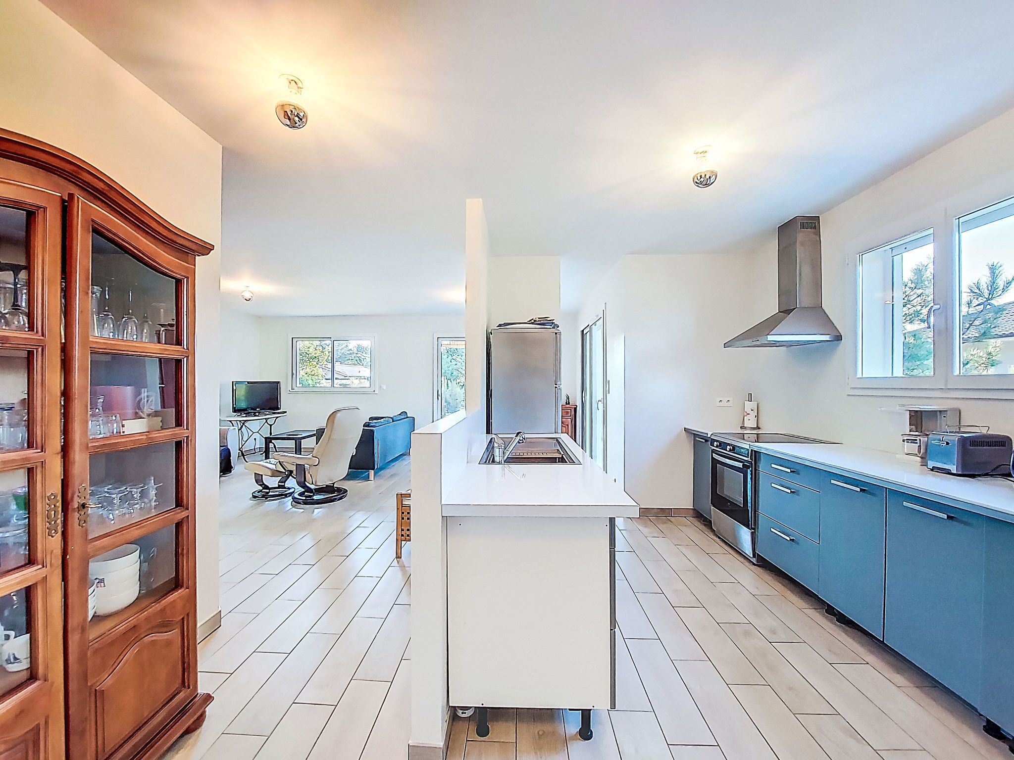 Une cuisine moderne dotée d’un îlot central, de meubles bleus et d’un meuble en bois avec des portes en verre.
