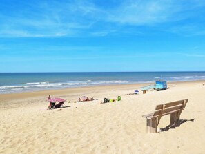 A beach with a lifeguard tower, a wooden bench, and people relaxing.