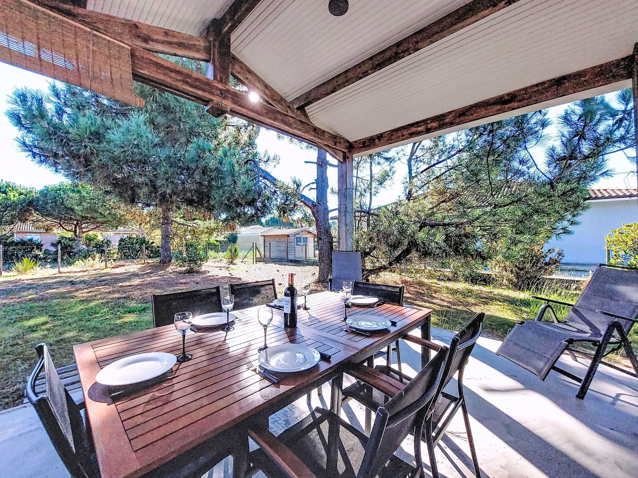 An outdoor dining area with a wooden table set for two, surrounded by chairs.