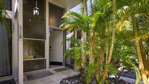 A modern building with a glass door, a number '118' on the wall, and a small garden with palm trees. - Aloha Condos, Keauhou Resort, Condo 118, Ocean View, AC (Kailua Kona)