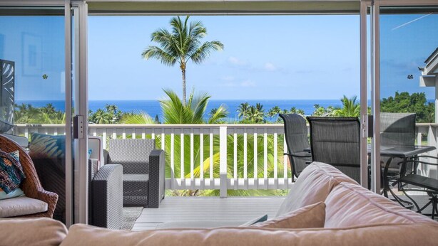 A balcony with a white railing, wicker furniture, and a view of the ocean and palm trees. - Aloha Condos, Keauhou Resort, Condo 118, Ocean View, AC (Kailua Kona)