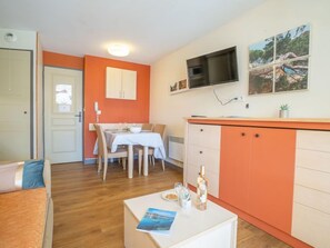 Espaço compacto com área de refeições, cozinha compacta e TV fixada na parede.