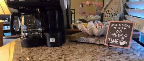 Una cafetera sobre una encimera de cocina, con un cartel que dice 'Rise & Shine It's Coffee Time'.