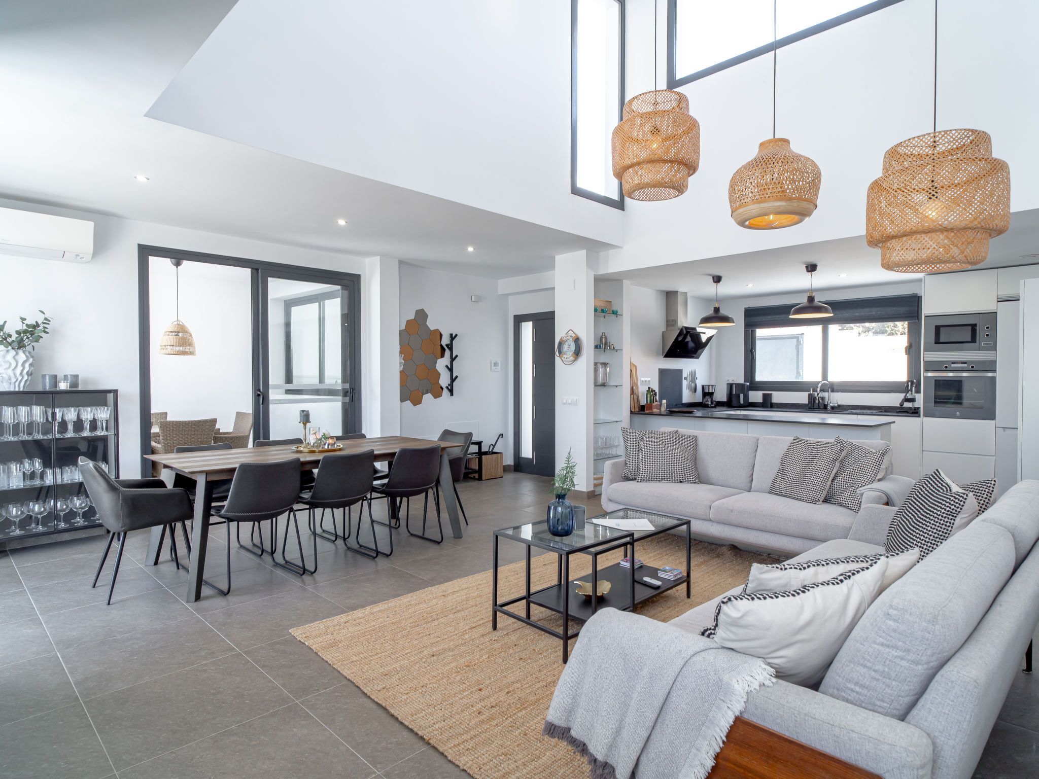 Uma sala de estar moderna com um sofá cinzento, uma mesa de centro e uma área de jantar com cadeiras e uma mesa.