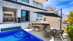 Un espace de vie extérieur moderne, doté d’une piscine, de mobilier d’extérieur et d’un coin salon abrité.