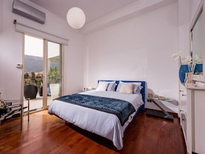 Quarto moderno com uma cama grande, uma porta de vidro deslizante que dá para uma varanda e vista para o exterior.