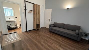 A modern living room with a grey sofa, wooden flooring, a built-in bench, and a wall-mounted light fixture.