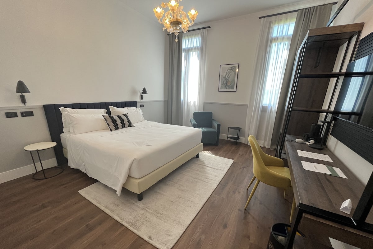 Ein modernes Hotelzimmer mit einem großen Bett, einem Schreibtisch, einem Sessel und einer Kristallleuchtre.