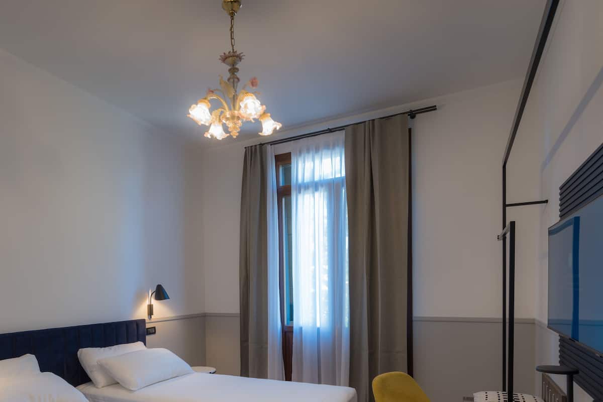Ein Hotelzimmer mit zwei Betten, einem Schreibtisch, einem Sessel, einem Fernseher und einer Kandelaber.