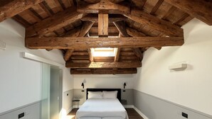 A narrow hallway leading to a bedroom with a large bed, a bench, and a skylight above. - The Foscarini (Mogliano Veneto)