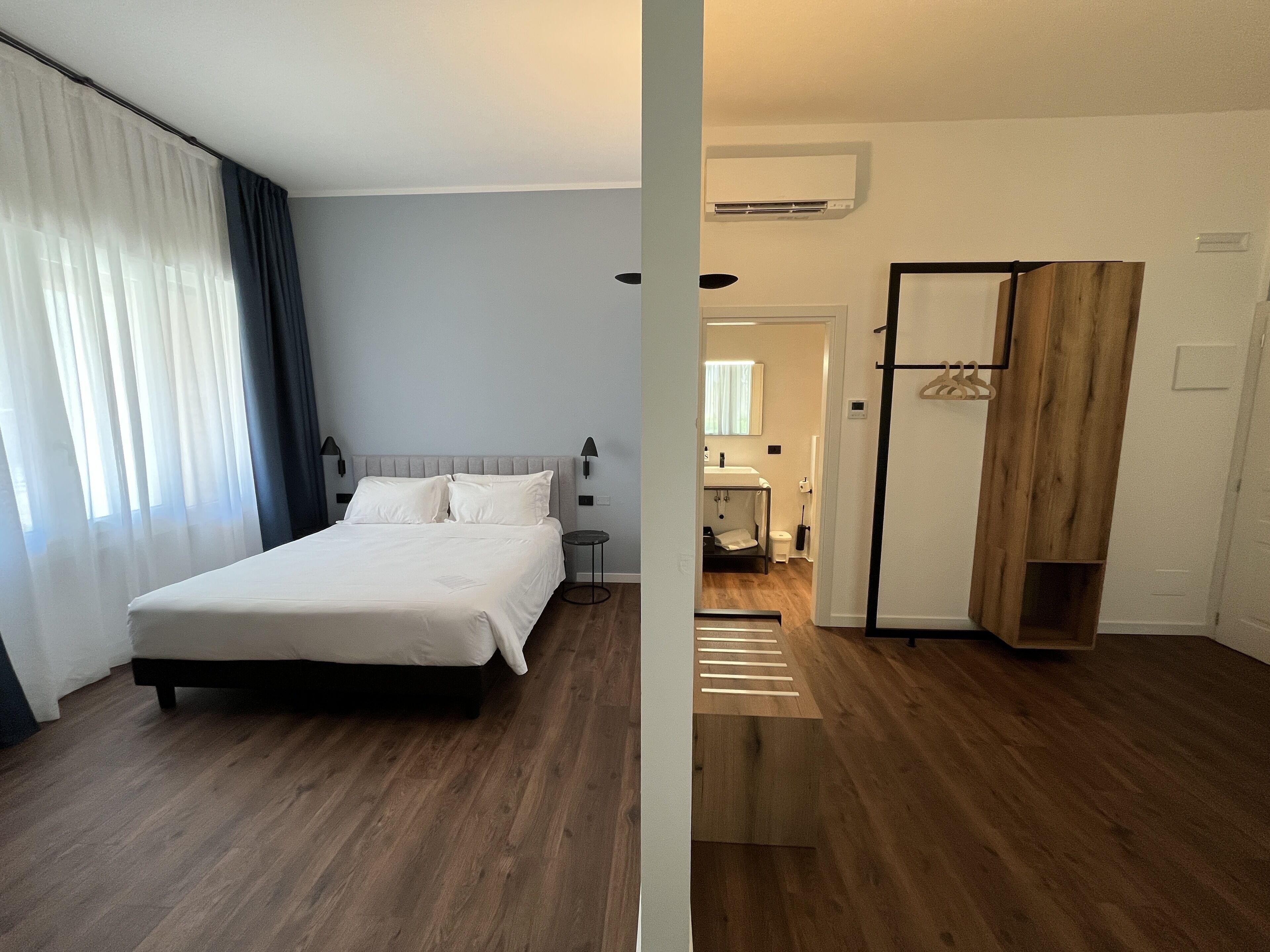 Une chambre d’hôtel avec un lit, une petite table de chevet, une armoire et une salle de bain visible à travers une porte ouverte.