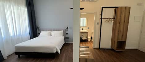 Une chambre d’hôtel avec un lit, une petite table de chevet, une armoire et une salle de bain visible à travers une porte ouverte.