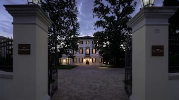 Een statig entree met een geplaveid pad dat leidt naar een gebouw met veel ramen en een bordje met de tekst 'The Foscarini'.