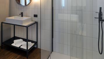Ein modernes Badezimmer mit einer gläsernen Duschkabine, einem weißen Waschbecken mit schwarzem Wasserhahn und einem Spiegel mit Wandleuchten.