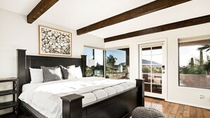 Une chambre moderne avec un grand lit, des poutres en bois, une cheminée et une vue sur l’extérieur.