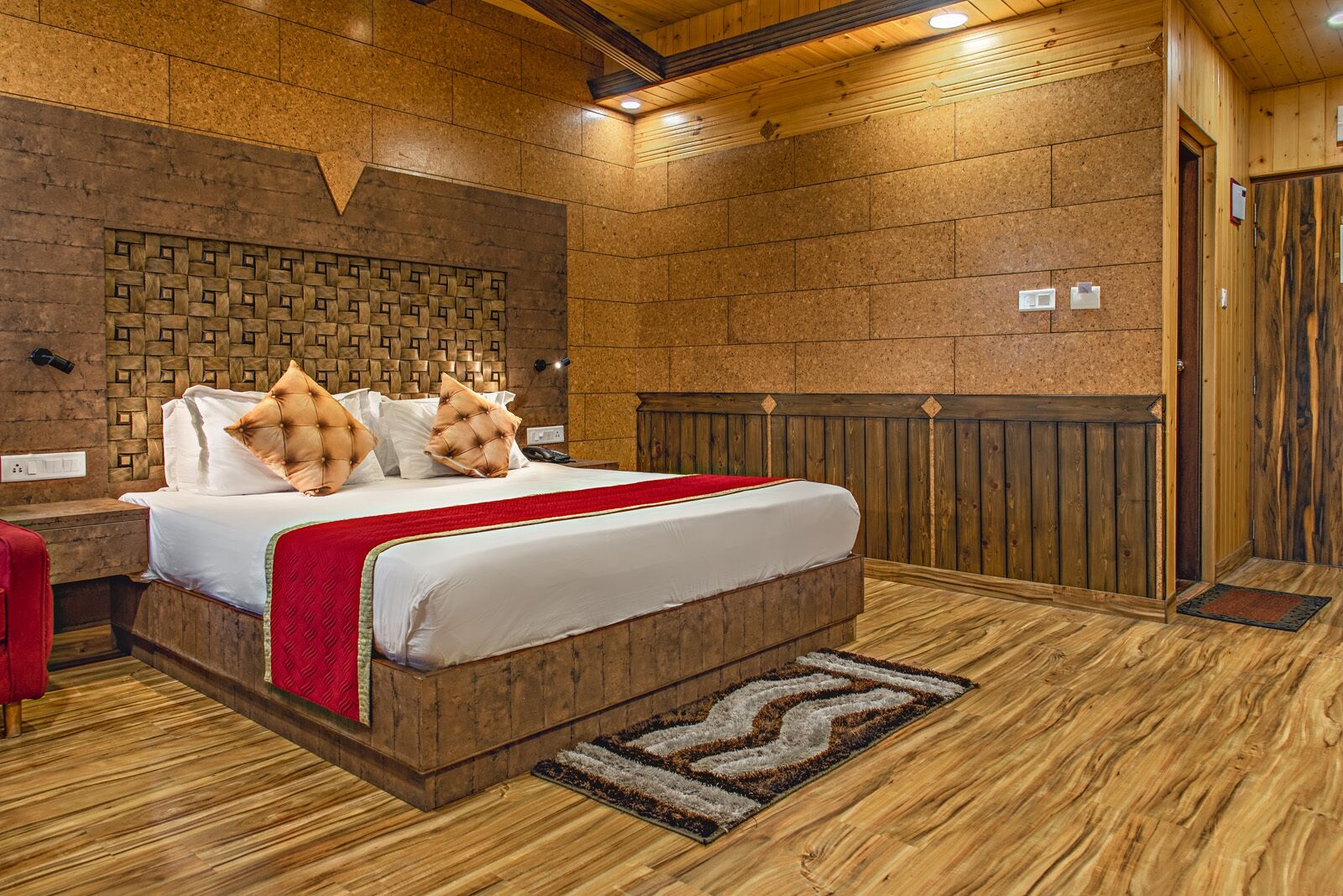 A bedroom with a wooden headboard, a large bed with a red throw blanket, and a patterned rug.