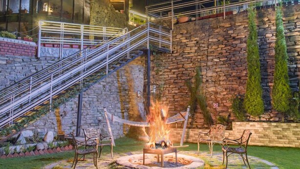 A stone building with a circular glass enclosure, a fire pit, and outdoor seating. - Kanishka Retreat Resort Chail (Kandaghat)