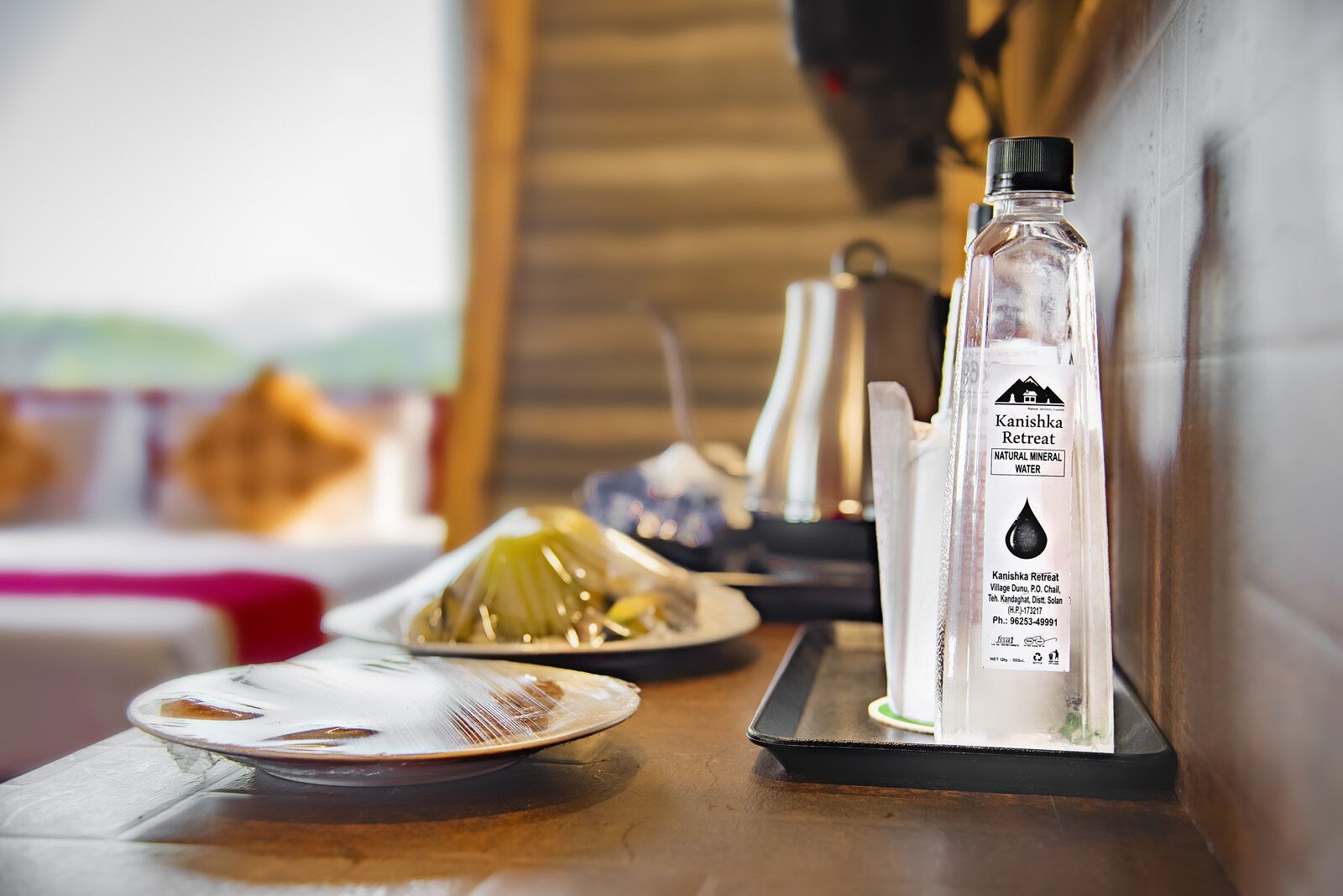 A bottle of Kanishka Retreat mineral water on a tray with a plate of food and a napkin dispenser.