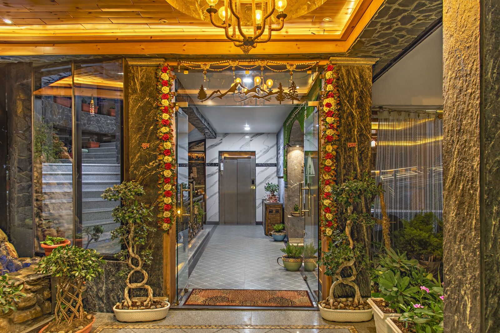 Entrada de hotel con piso de mármol, un candelabro y plantas en macetas.