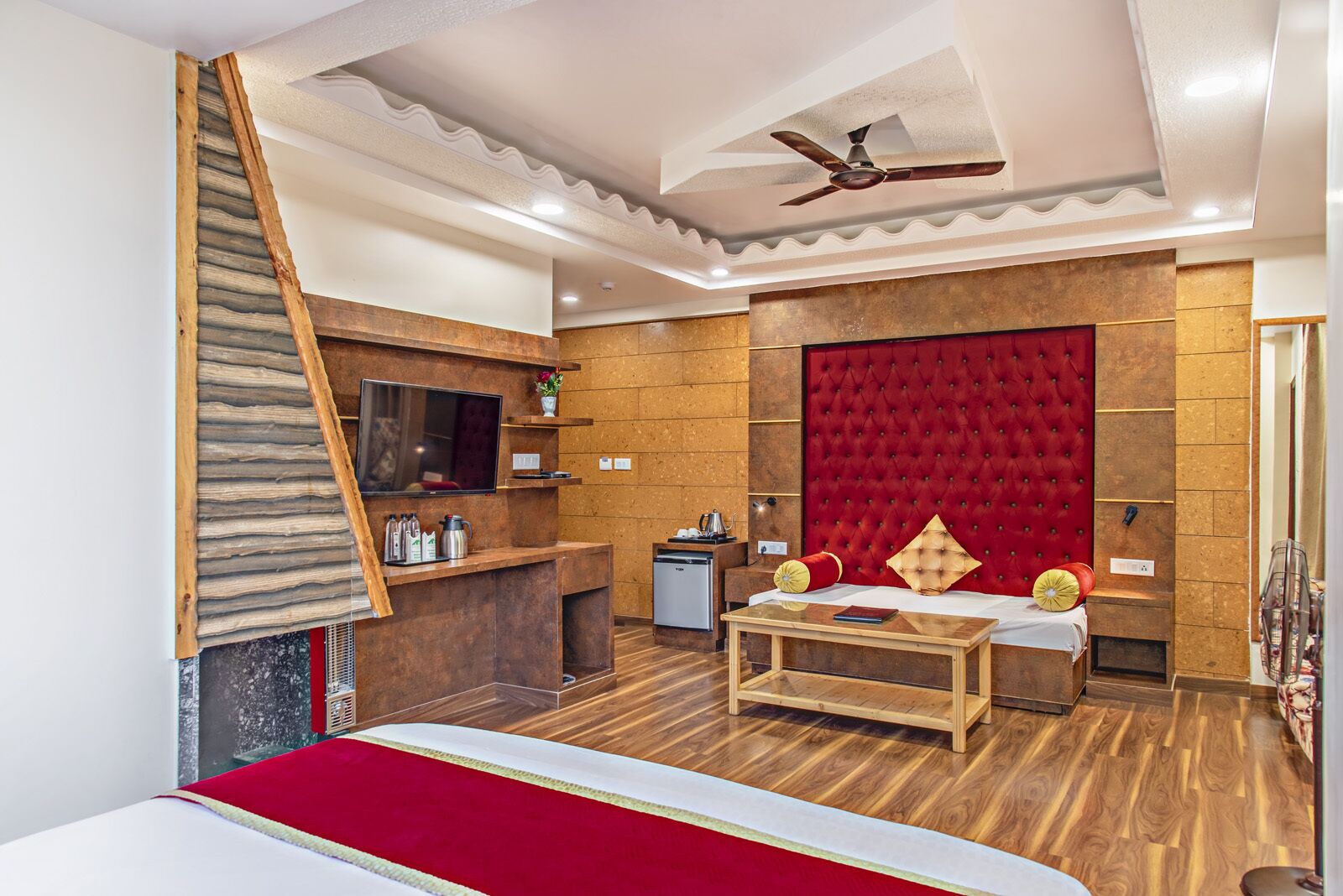 Habitación de hotel con escalera de madera, cabecera de terciopelo rojo, mesa de centro de madera y televisor montado en la pared.
