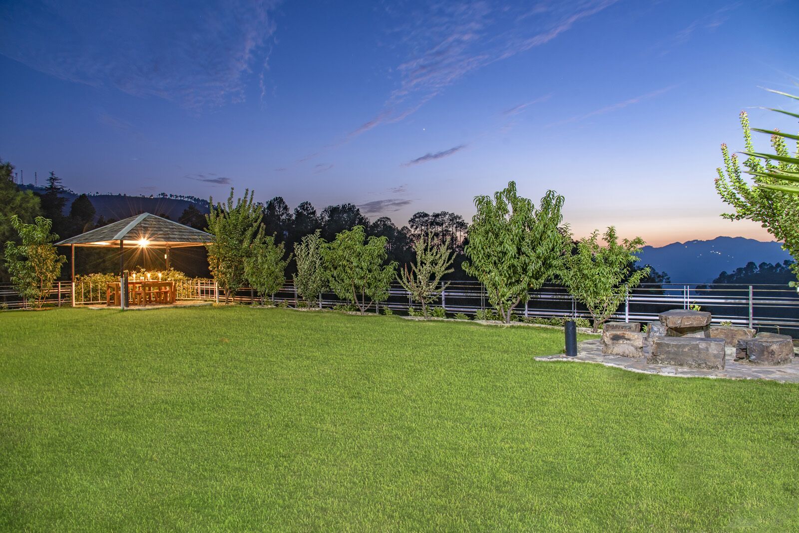 A well-lit outdoor area with a covered seating area, a grassy lawn, and a view of distant mountains.