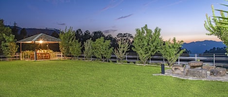 A well-lit outdoor area with a covered seating area, a grassy lawn, and a view of distant mountains.
