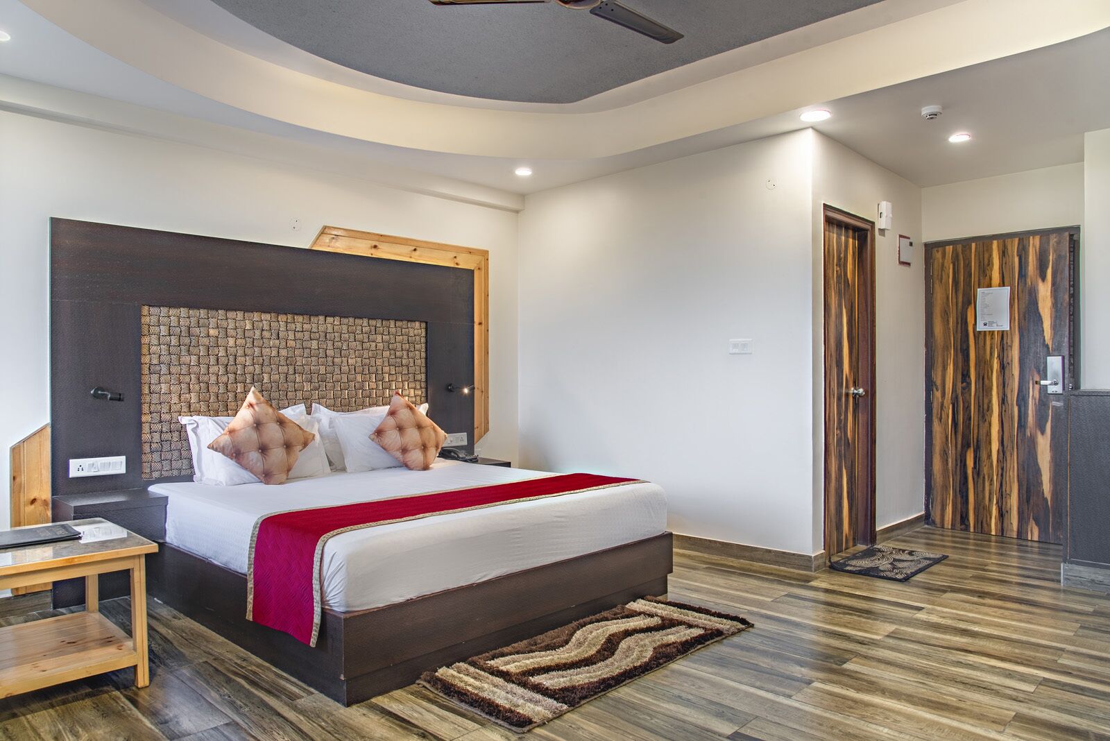 Una habitación de hotel moderna con una cama grande, un cabecero de madera, una mesita de noche y una mesilla.