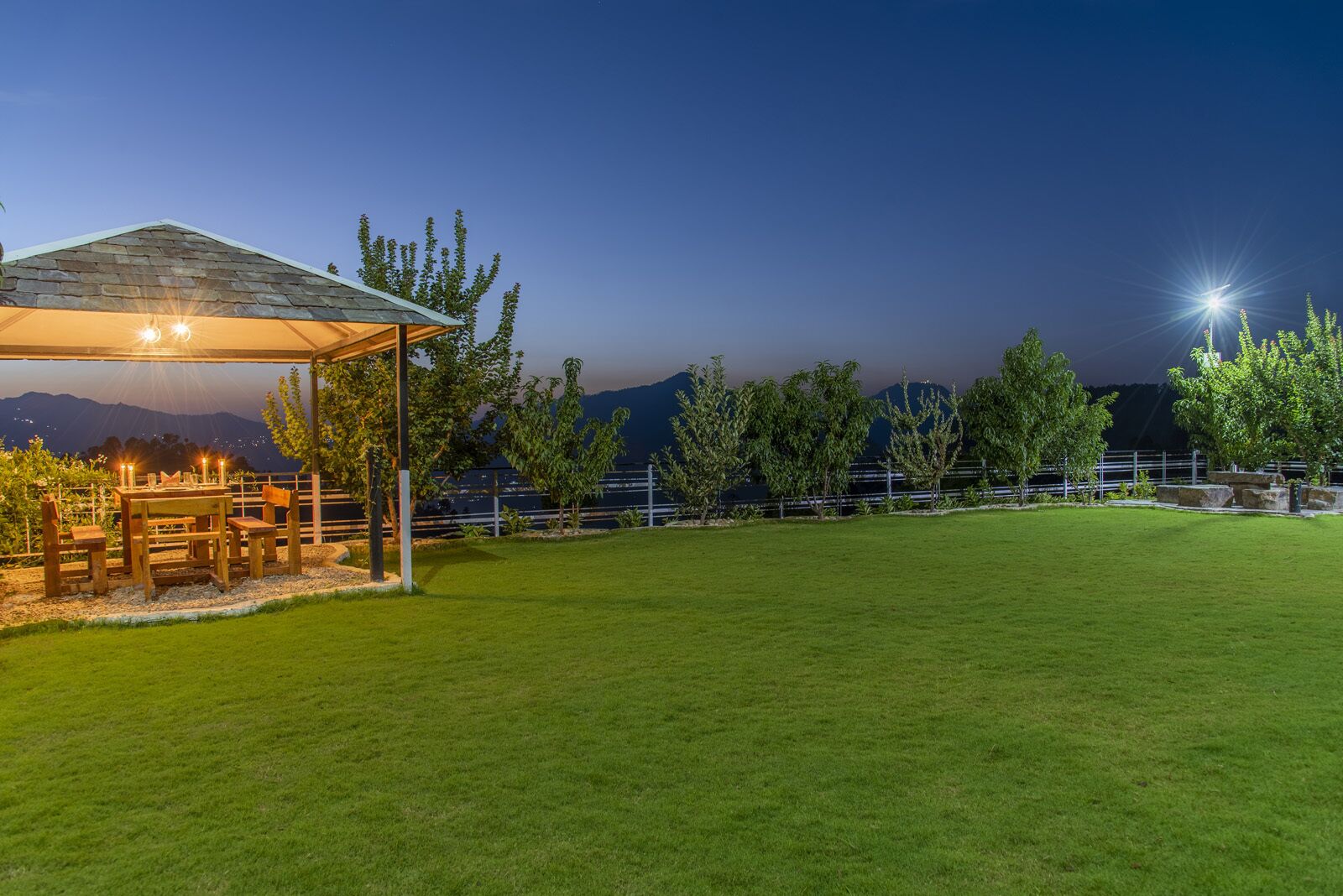 Un patio al aire libre bien iluminado con una mesa y sillas, rodeado de césped y una cerca.