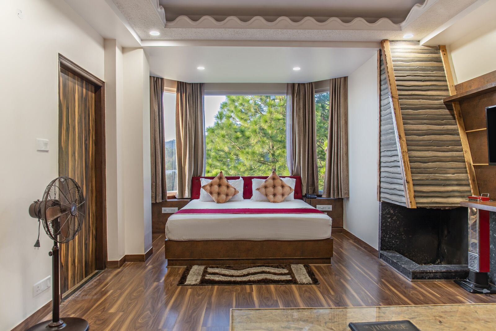 Une chambre avec un grand lit, une cheminée et une vue sur les arbres par la fenêtre.