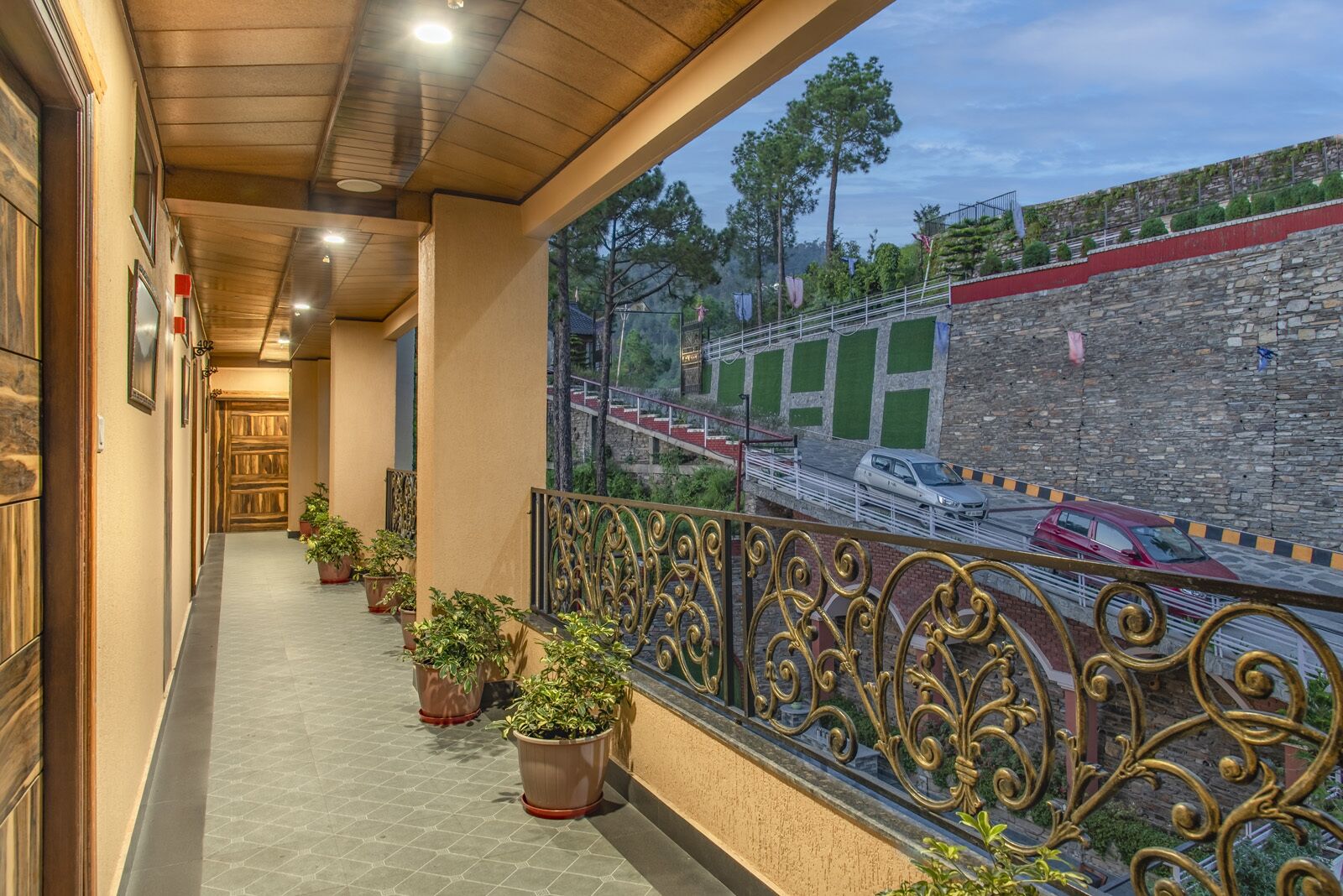 A corridor with potted plants, a decorative railing, and a mural of a train on a stone wall.