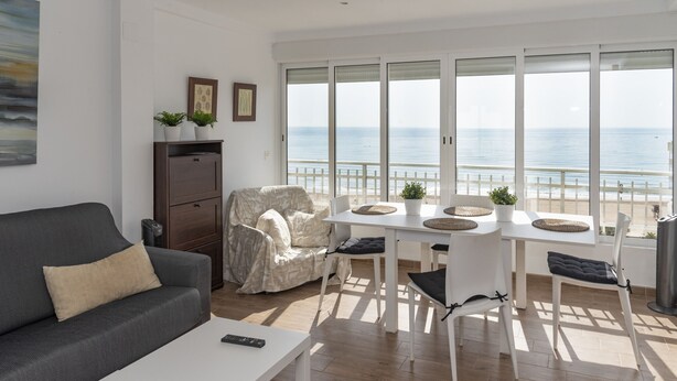 Ein modernes Wohnzimmer mit einer Couch, einem Esstisch mit Stühlen, einem abgedeckten Stuhl und Meerblick durch große Fenster.
