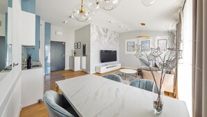 Un salon moderne doté d’une table à manger en marbre, d’un téléviseur à écran plat et d’un coin salon avec un canapé et des fauteuils.