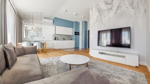 Un salon moderne avec un canapé gris, une table basse blanche et un téléviseur à écran plat posé sur un meuble de télévision blanc.
