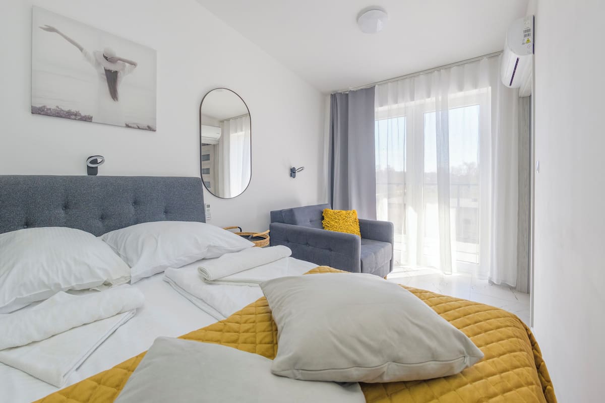 A modern hotel room with a large bed, a sofa, a mirror, and a window with curtains.