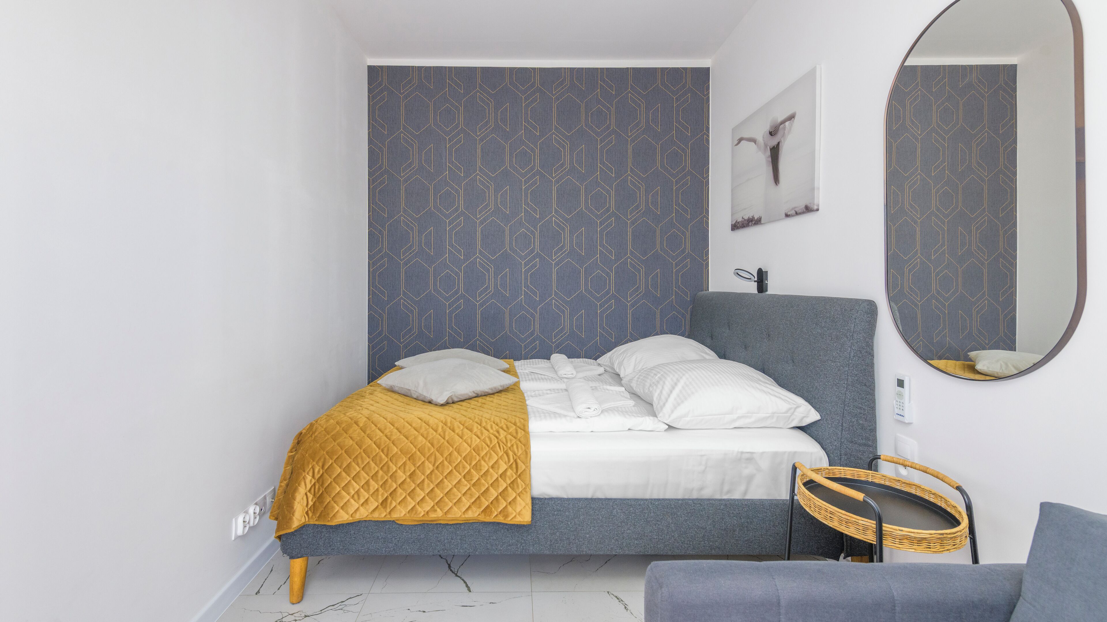 A modern bedroom with a bed, a bedside table, a mirror, and a wall-mounted light.