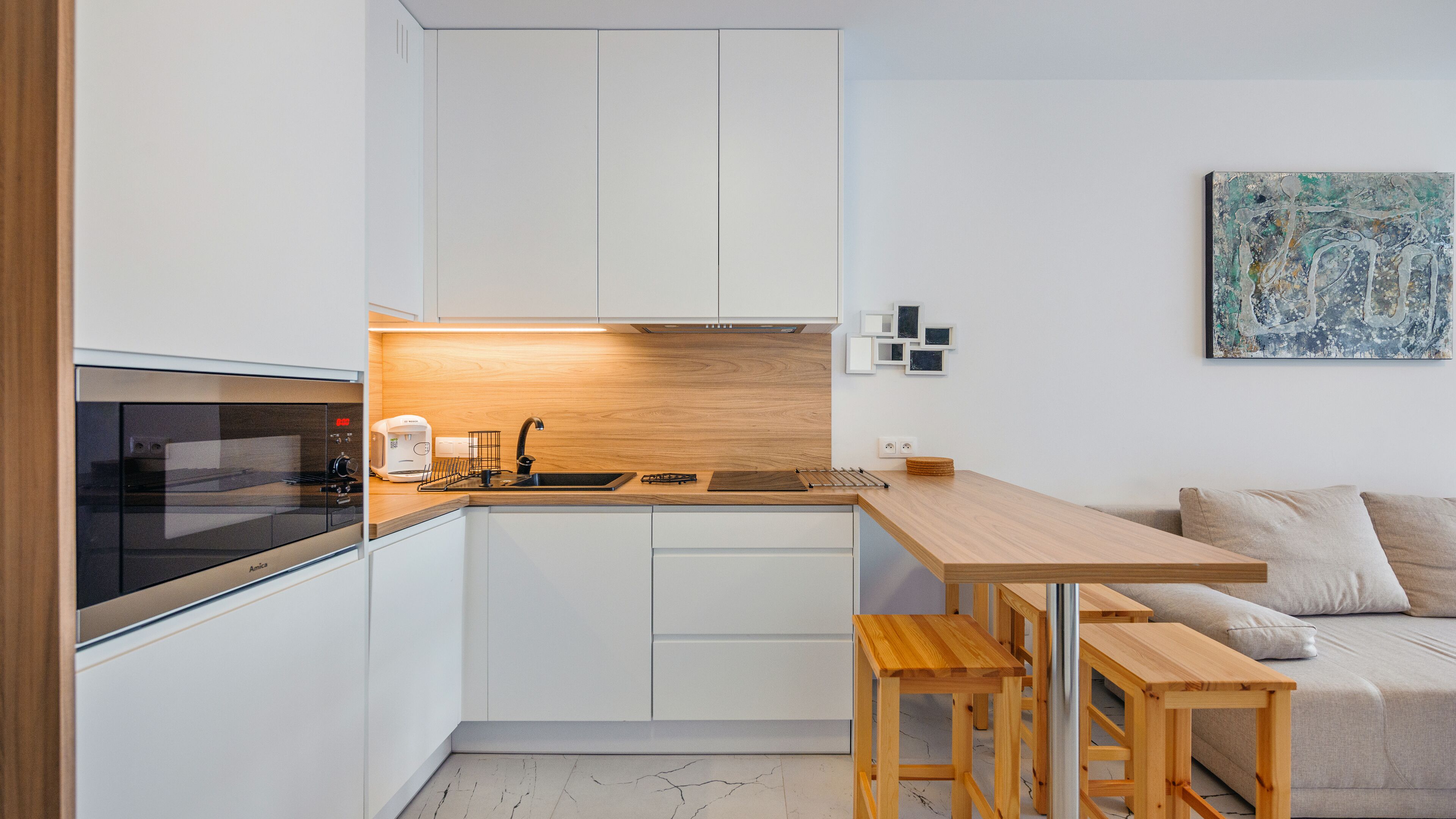 Une cuisine compacte équipée d’un four à micro-ondes, d’un grille-pain et d’un évier. On y trouve une table et un banc en bois, ainsi qu’un canapé dans le salon attenant.