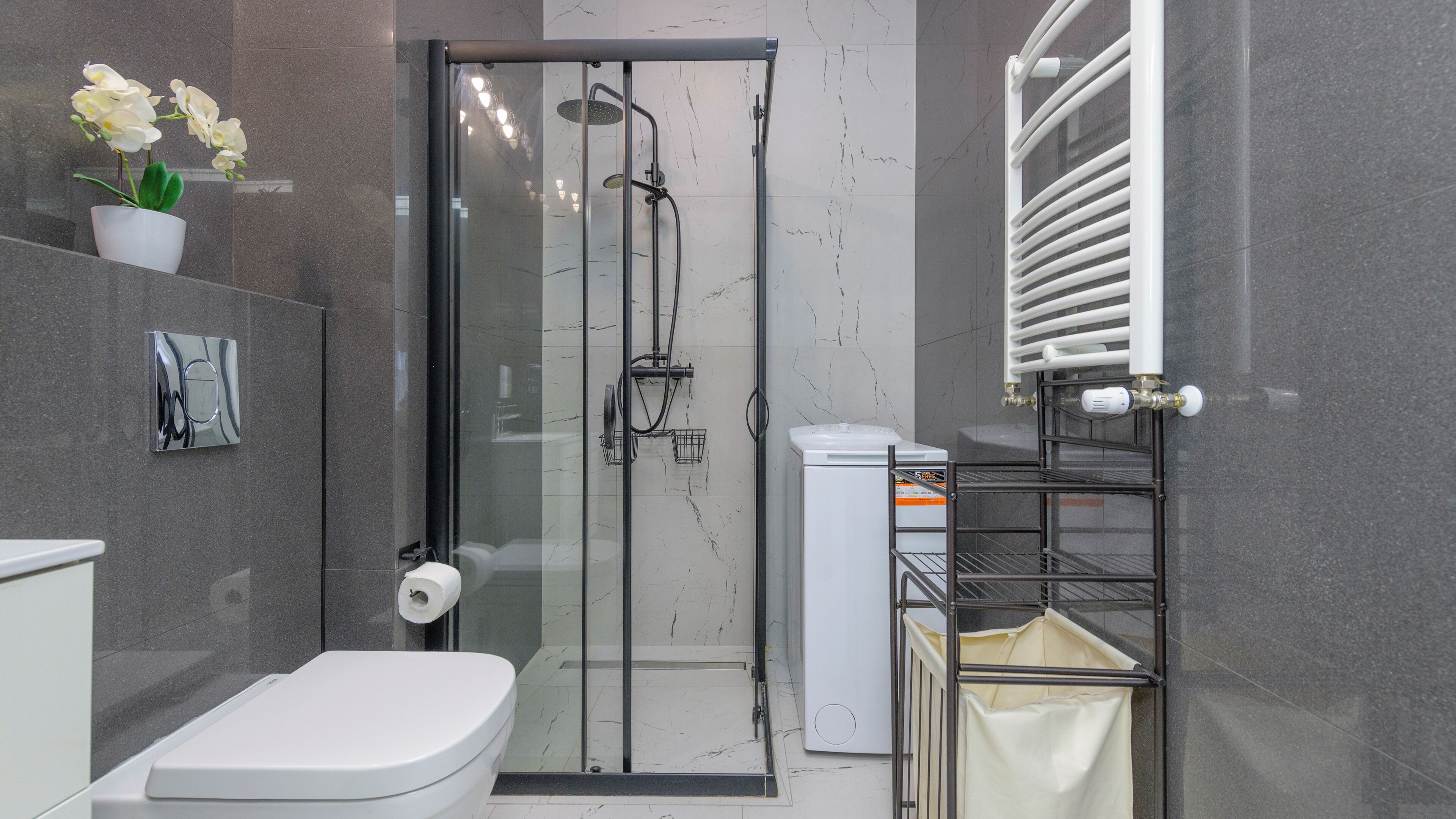 A modern bathroom with a glass-enclosed shower, a toilet, a towel rack, and a shelf with a potted plant.