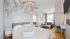 Une chambre moderne avec un grand lit, un coin salon comprenant un fauteuil et un pouf, et un petit bureau.