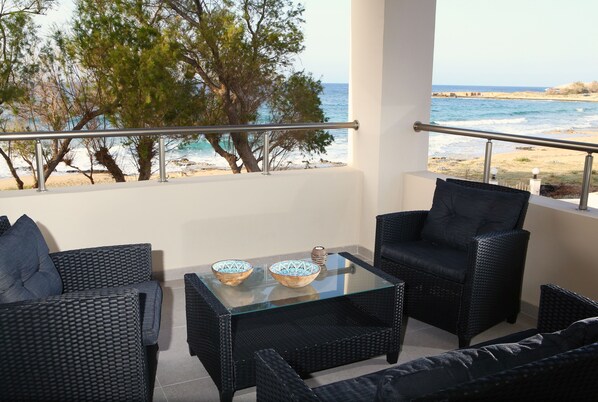 Un balcón con mobiliario de mimbre, una mesa de vidrio y vista a la playa y al océano.
