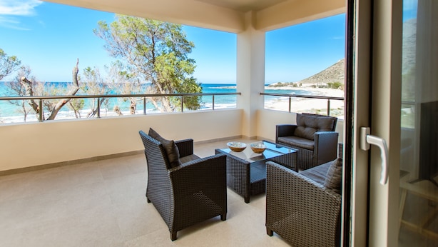 Un balcón con mobiliario de mimbre, una mesa de vidrio y vistas a la playa y al océano.