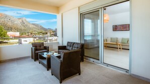 Un balcón con mobiliario de mimbre, una puerta de cristal que da a una zona de estar interior y vistas a la montaña.