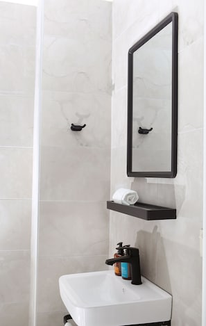 Un baño con un lavamanos blanco, un espejo, un perchero para toallas y un dispensador de jabón.