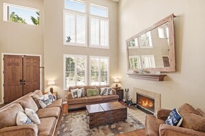 A spacious living room with a fireplace, large windows, and a mirror on the wall.